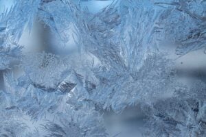 Intricate ice crystals and frost formations covering a window pane in blue and white tones.